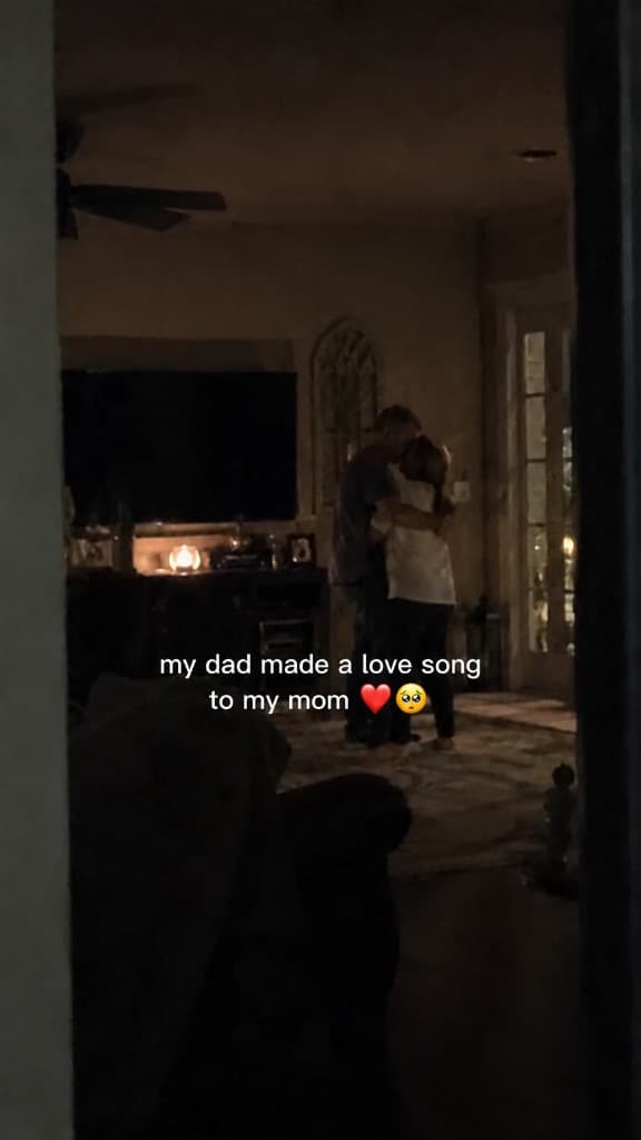 A couple holding each other in a dim living room while a love song plays